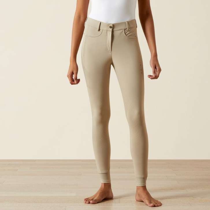 Woman wearing beige pants and a white top on a plain background