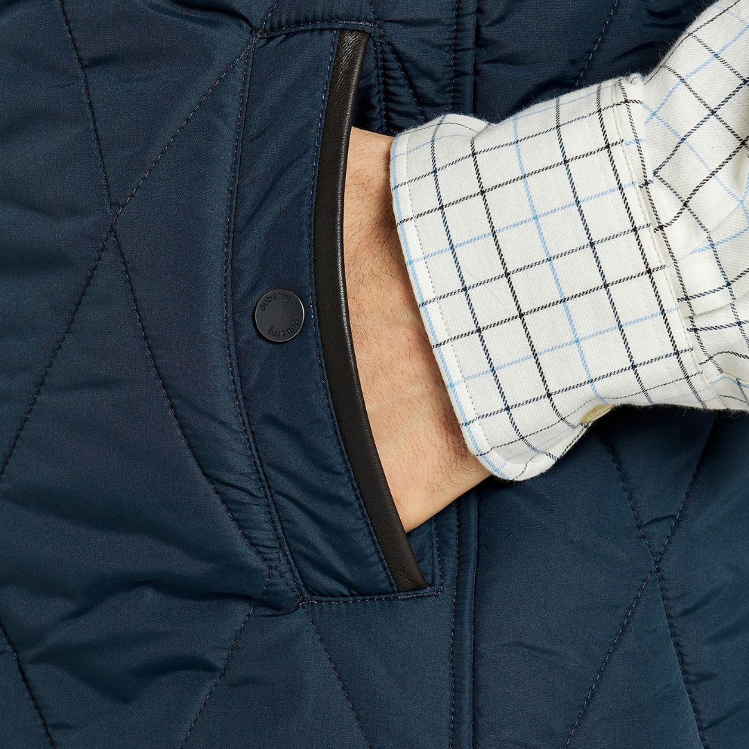 Close-up of a navy blue quilted jacket with a checkered shirt sleeve peeking out.