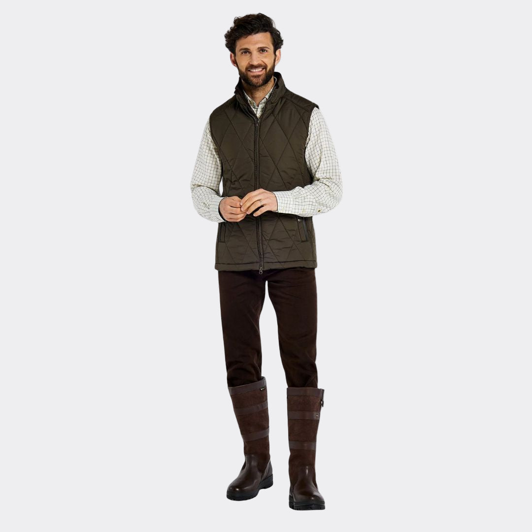 Man wearing a green vest, checkered shirt, dark pants, and boots on a white background
