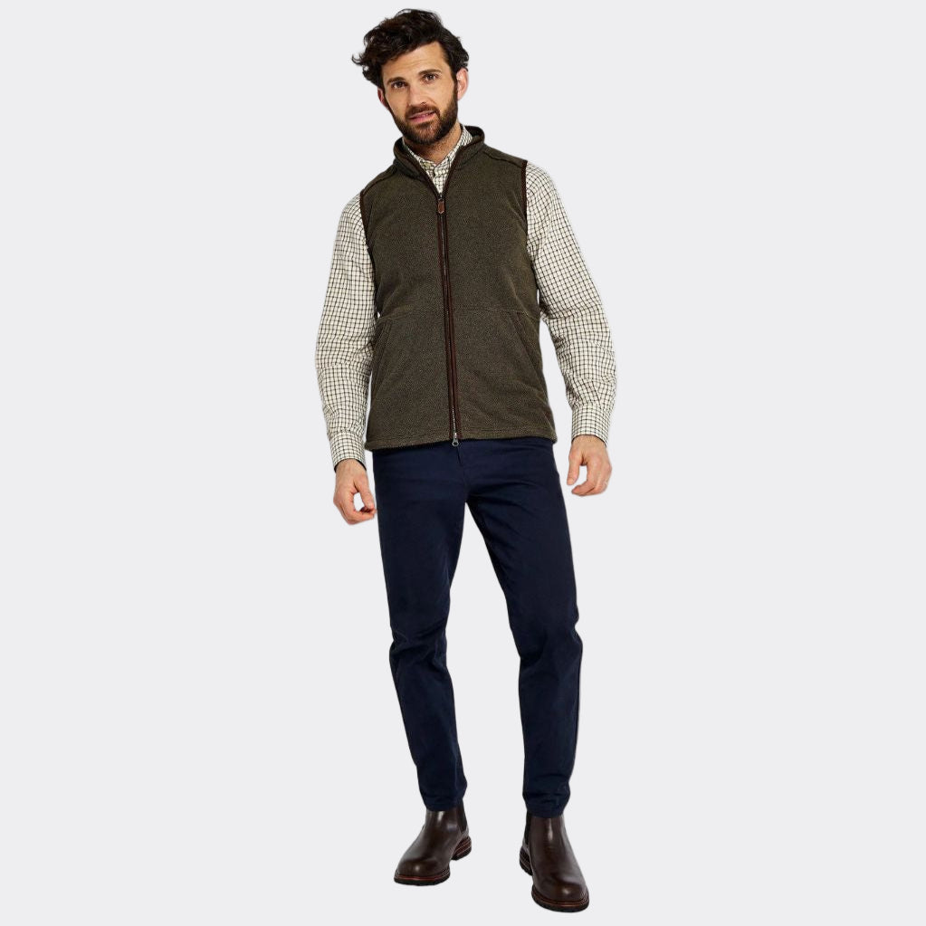 Man wearing a brown vest over a checkered shirt with navy pants on a white background