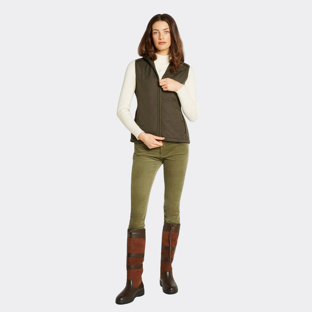 Woman wearing a green vest, white shirt, green pants, and brown boots on a white background