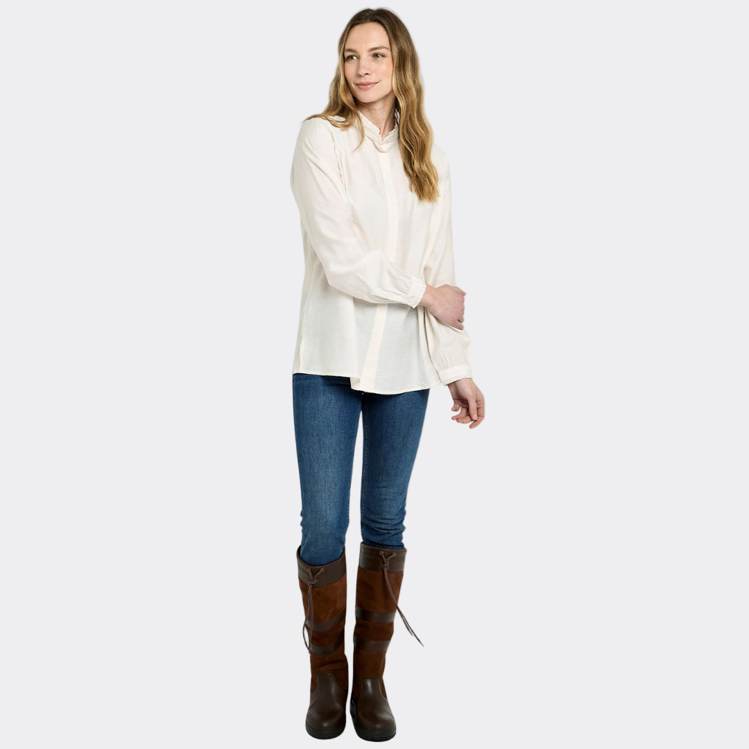 Woman wearing a white blouse, blue jeans, and brown boots on a white background