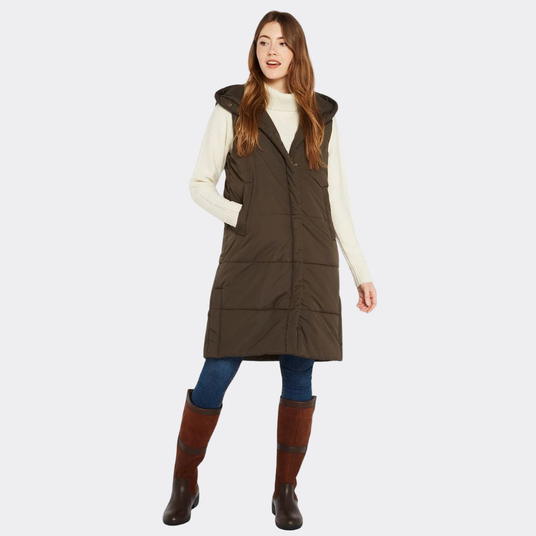 Woman wearing a brown puffer vest over a white shirt with blue jeans and brown boots on a white background