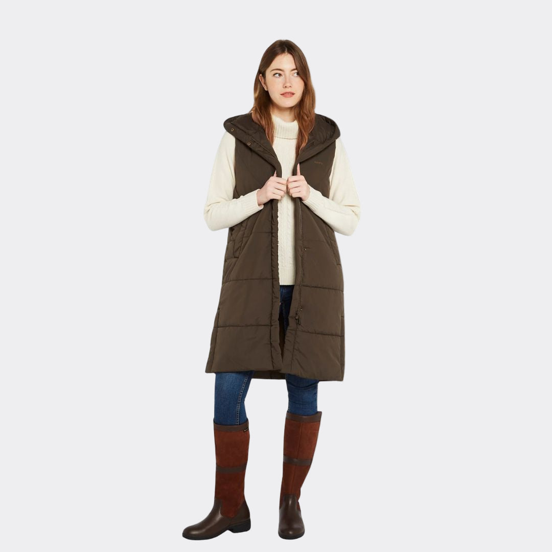 Woman wearing a long brown puffer vest over a white sweater on a white background