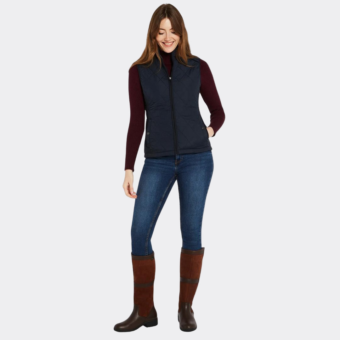 Woman wearing a navy vest, maroon long-sleeve shirt, blue jeans, and brown boots on a white background