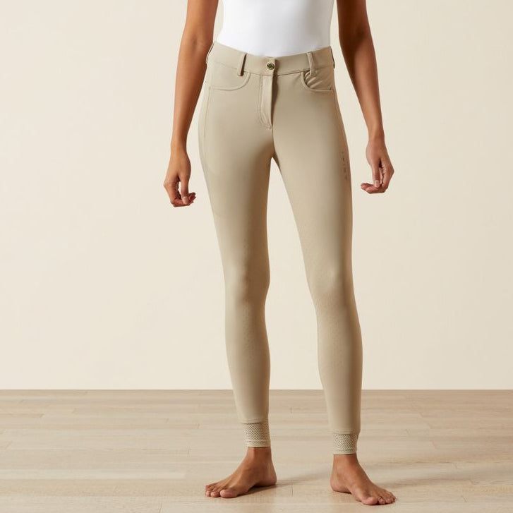 Woman wearing beige pants and a white top on a plain background