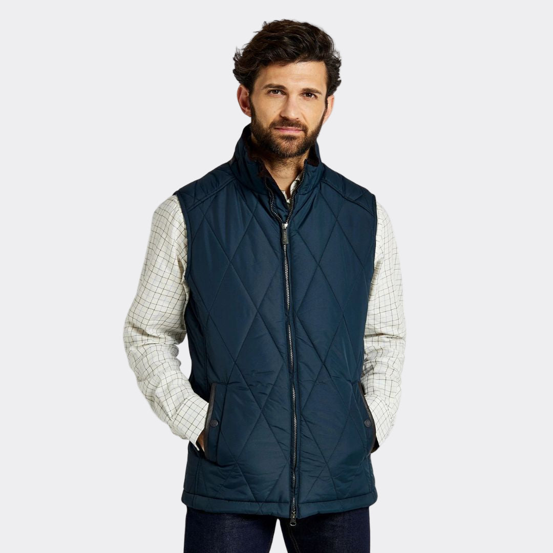 Man wearing a navy quilted vest over a plaid shirt on a white background