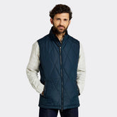 Man wearing a navy quilted vest over a plaid shirt on a white background