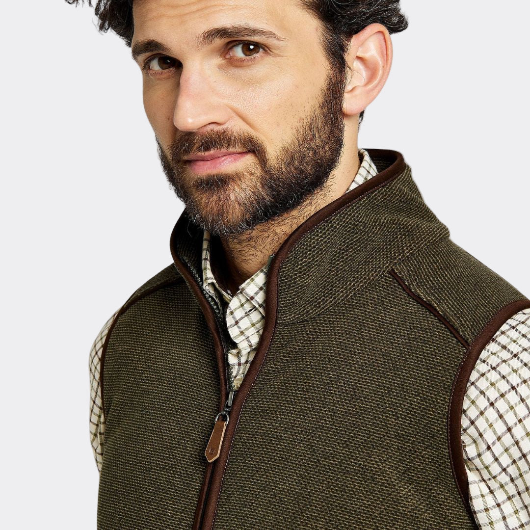 Man wearing a green vest over a plaid shirt on a white background