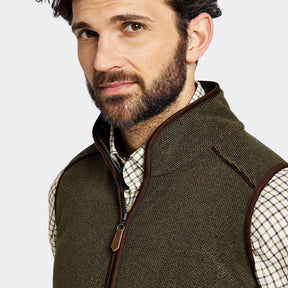 Man wearing a green vest over a plaid shirt on a white background