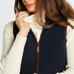 Person wearing a navy vest over a cream sweater with a white background