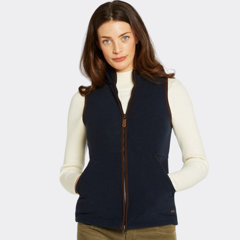 Woman wearing a navy blue vest over a white long-sleeve shirt on a white background