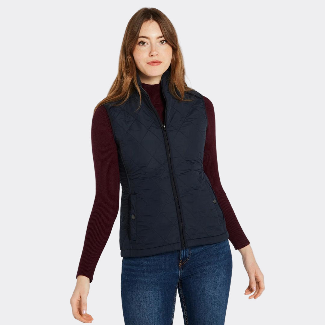 Woman wearing a navy puffer vest over a red long-sleeve shirt on a white background