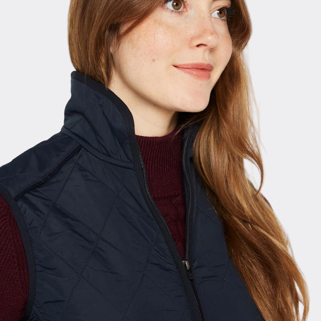 Woman wearing a navy quilted vest over a red sweater on a white background