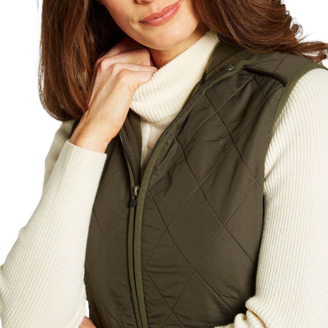 Woman wearing a green quilted vest over a white sweater on a white background