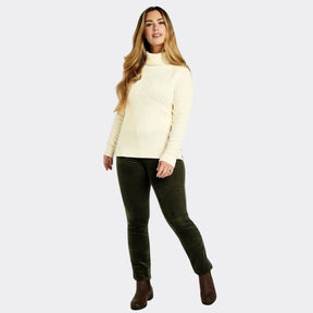 Woman wearing a cream sweater and dark green pants on a white background