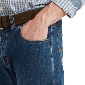 Close-up of a person wearing blue jeans with a Schott belt on a white background