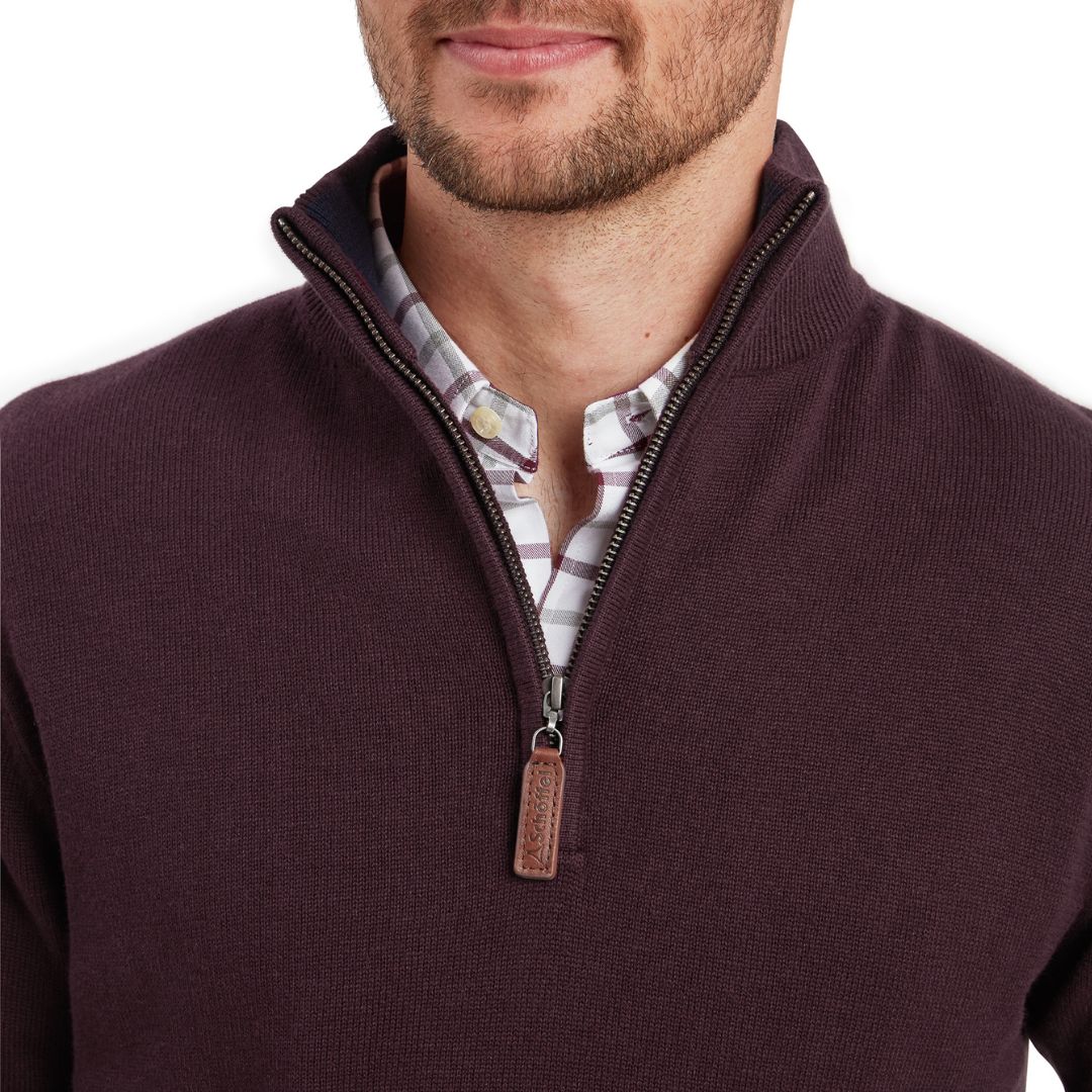 Man wearing a dark brown zip-up sweater over a patterned shirt on a white background