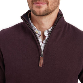Man wearing a dark brown zip-up sweater over a patterned shirt on a white background
