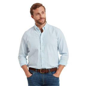 Man wearing a light blue button-up shirt and jeans on a white background
