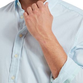 Person adjusting the collar of a light blue shirt on a white background