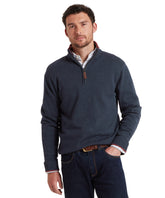 Man wearing a navy blue quarter-zip sweater and dark jeans on a white background